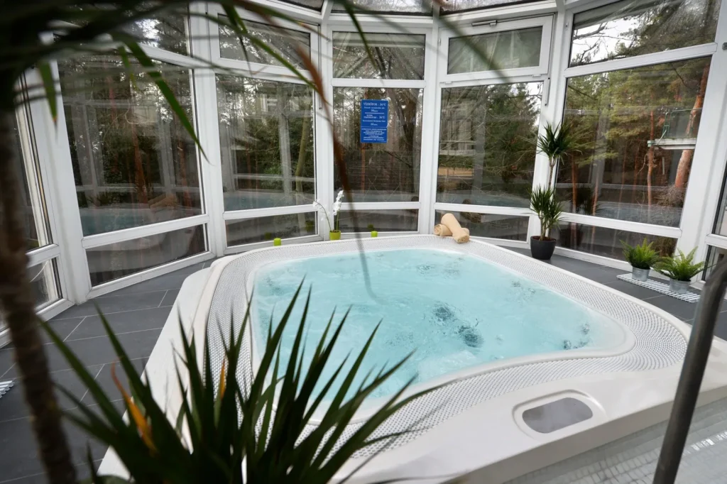 Üvegfalú pihenőtérben álló, buborékos jakuzzi növényekkel körülvéve